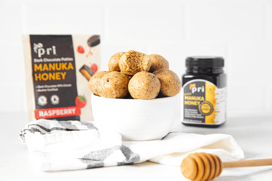 Manuka honey protein balls in a white bowl, with Manuka honey jar and raspberry honey snacks in background