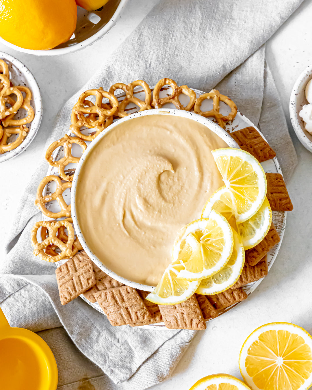 Creamy honey dip with lemon slices, pretzels, and crackers on a white plate
