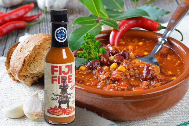 Fiji Fire chili sauce bottle beside spicy bean chili, fresh bread, garlic, and red chili peppers