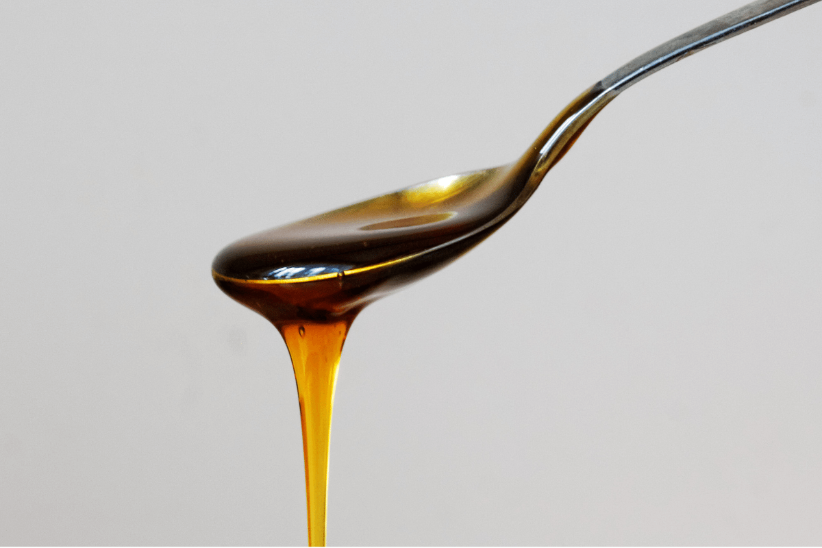 Golden Manuka honey dripping from a spoon against a light gray background.