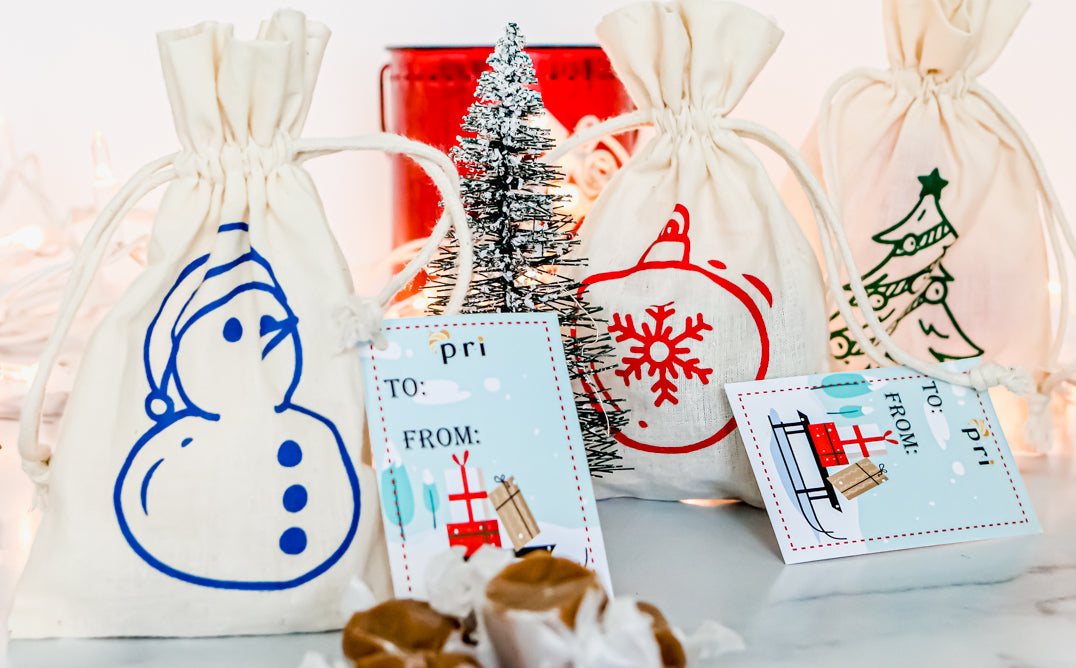 Holiday gift bags with festive prints, Christmas tree, gift tags, and soft caramels on white table.