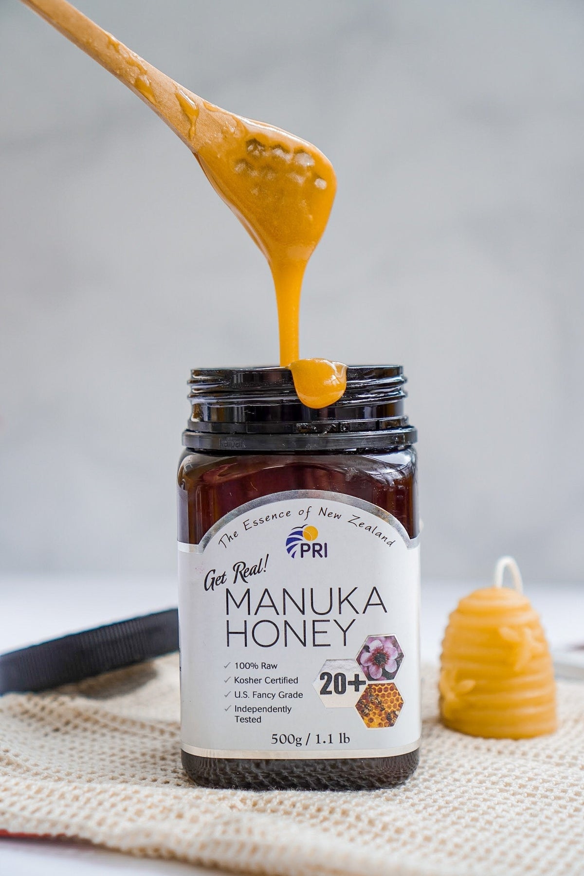 Jar of Manuka honey with honey dipper, label showing 20+ grade and raw New Zealand honey
