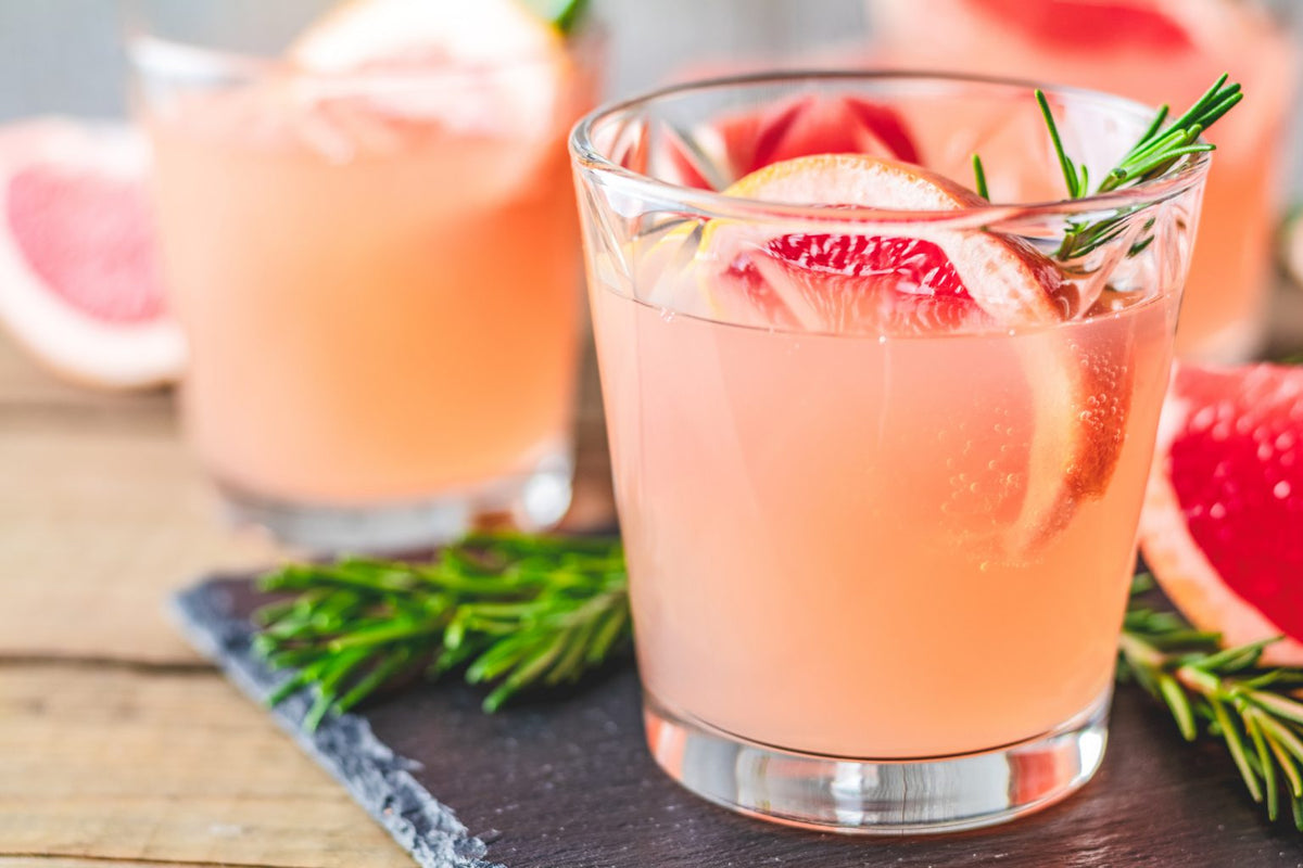 Glass of pink grapefruit honey drink with fresh grapefruit slices and rosemary garnish