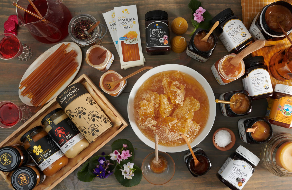 Assorted jars and sticks of Manuka honey, honeycomb in bowl, flowers, and honey dippers