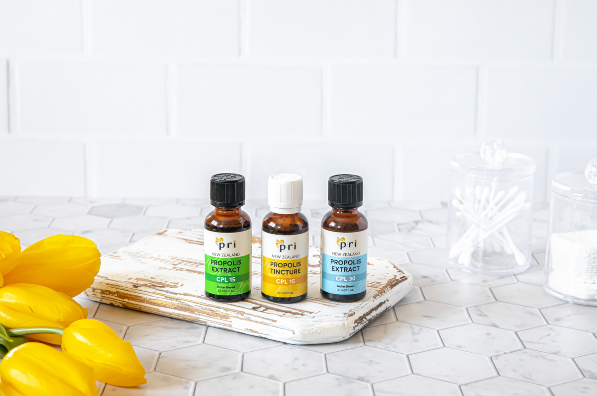 Three bottles of New Zealand propolis extract on tile counter with yellow tulips and cotton swabs