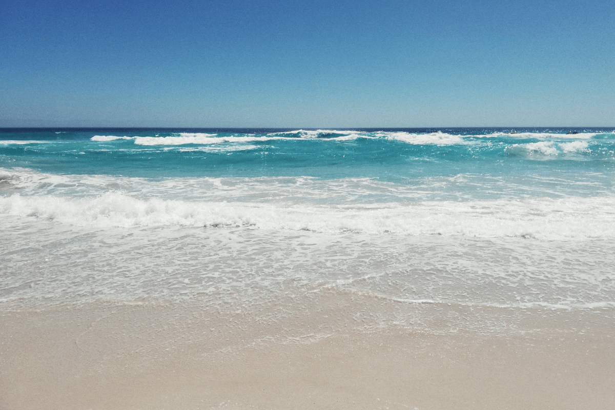 Peaceful ocean beach with turquoise water, gentle waves, and a sandy shoreline.
