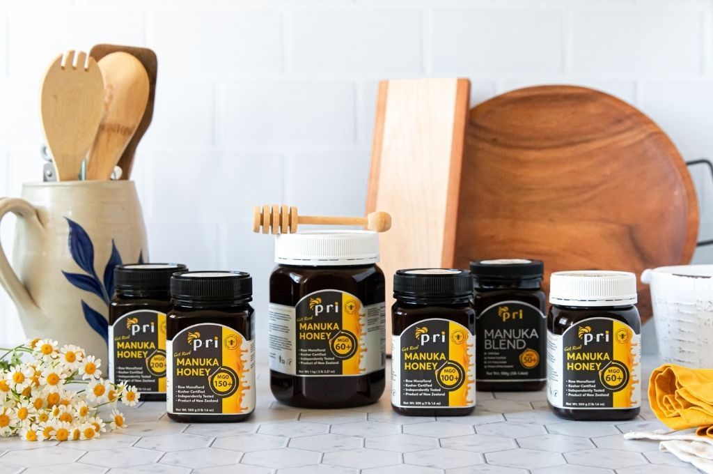 Assorted jars of Manuka honey on a kitchen counter with wooden utensils and chamomile flowers