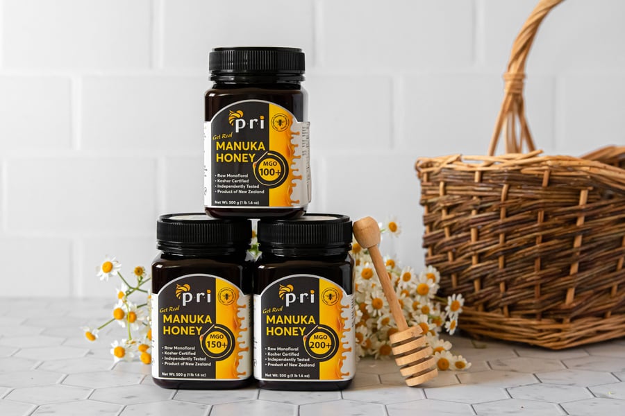 Jars of New Zealand Manuka honey with honey dipper, basket, and chamomile flowers