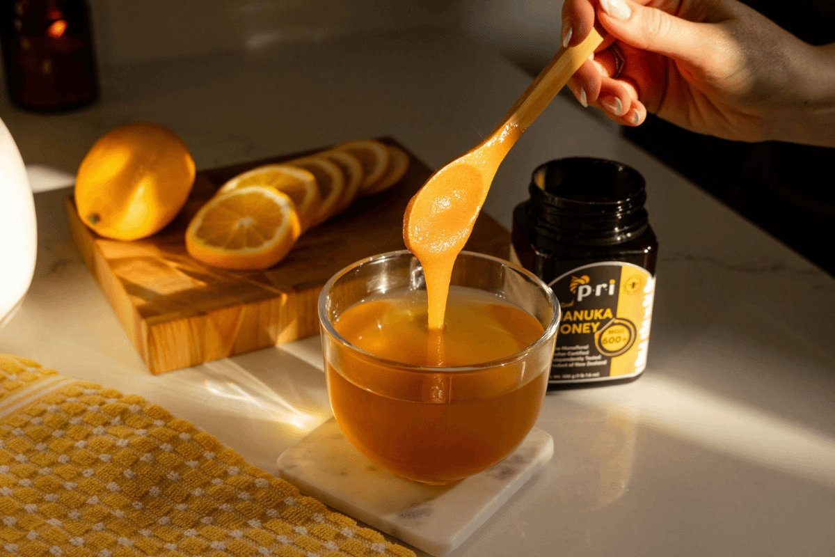 Manuka honey being poured into a glass jar with honey products in the background.