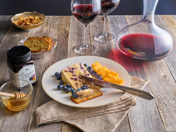 Charcuterie board with cheese, blueberries, honey, wine glasses, honey jar, and decanter