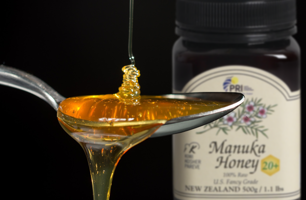 Spoonful of Manuka honey dripping, bottle of New Zealand Manuka honey in background