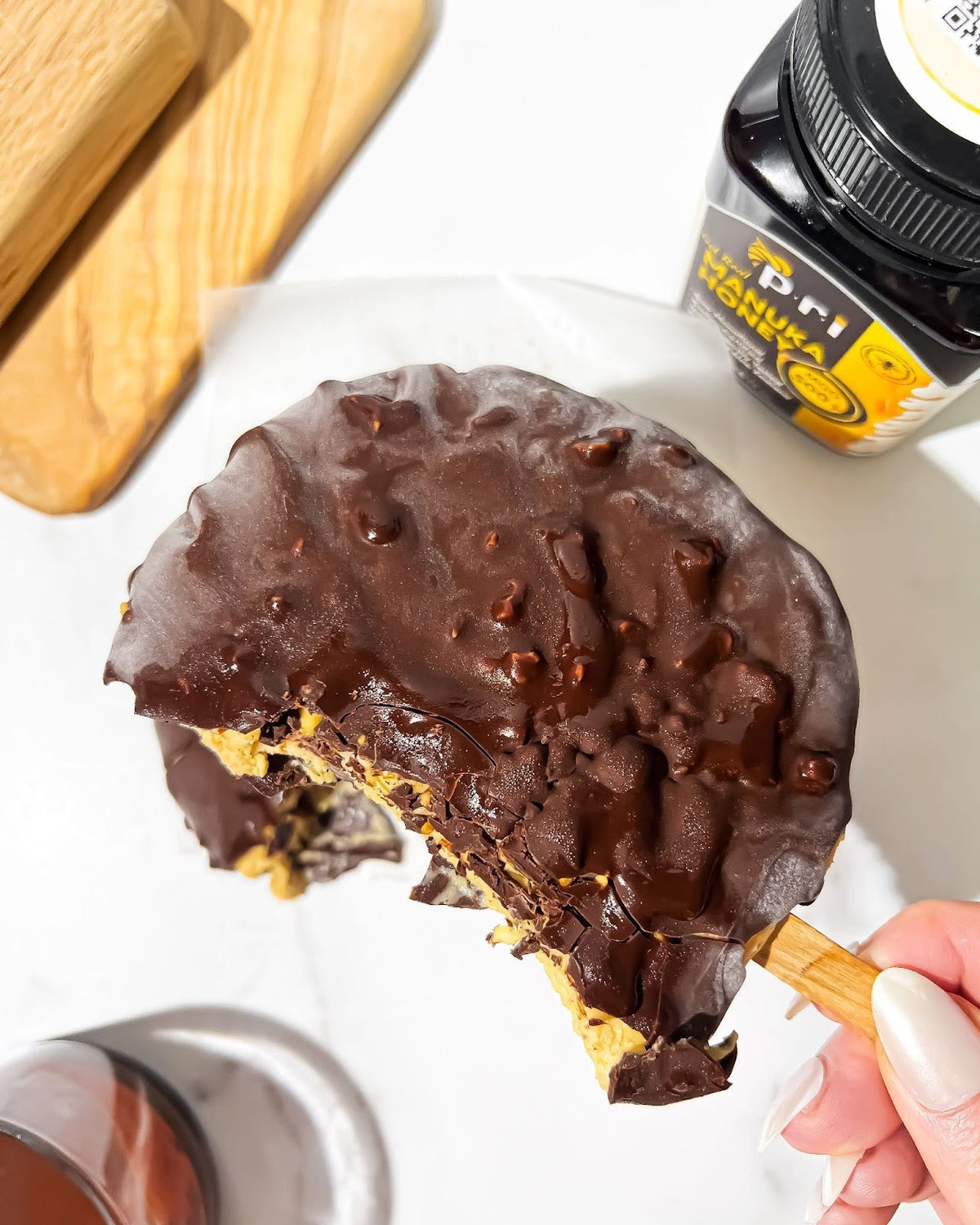 Hand holding chocolate-covered rice cake with peanut butter and Manuka honey jar